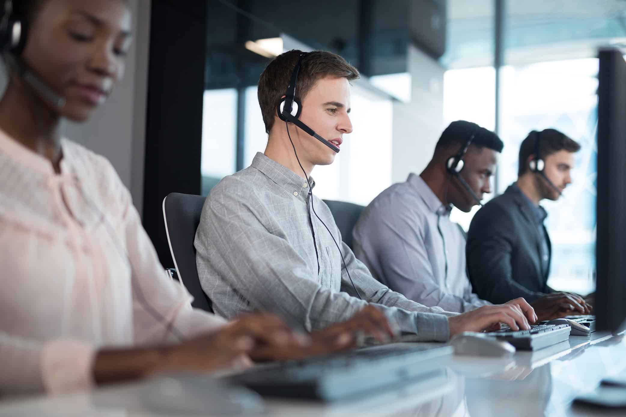 Four customer service technicians using headsets and computers