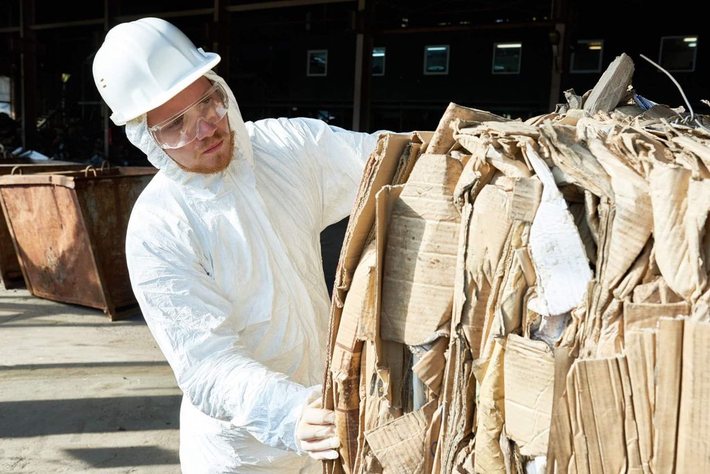 Worker in hazmat suit sorting cardboard at recycling plant